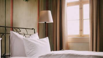 A neatly made bed with white linens in a room with a window, a lamp, and a wall with vertical stripes.