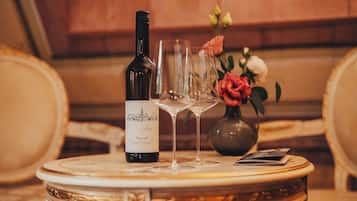 A bottle of wine, two glasses, and a vase with flowers on a round table.