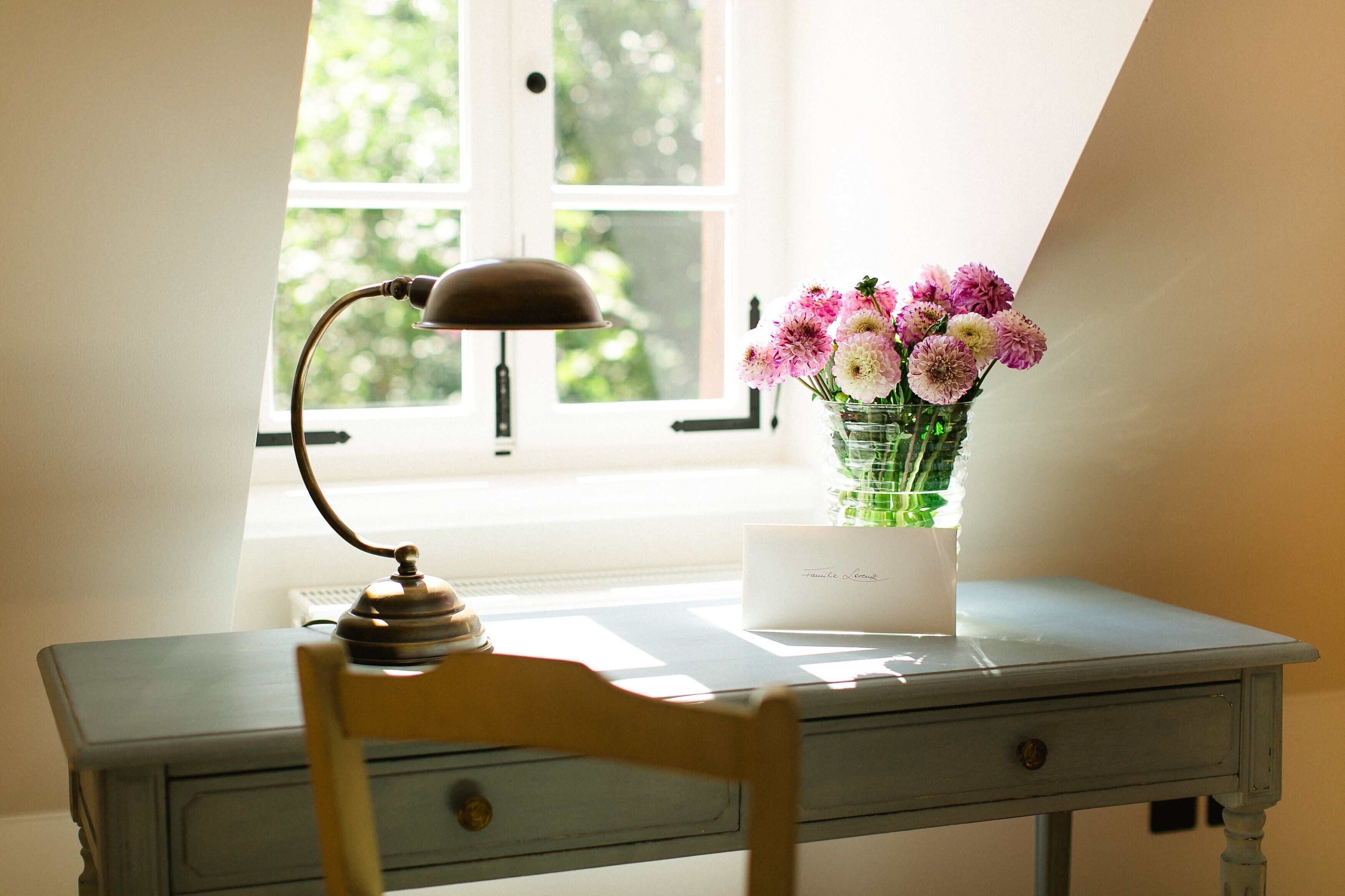 A desk with a lamp, a vase of flowers, and a card on it.
