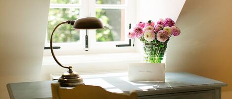 A desk with a lamp, a vase of flowers, and a card on it.
