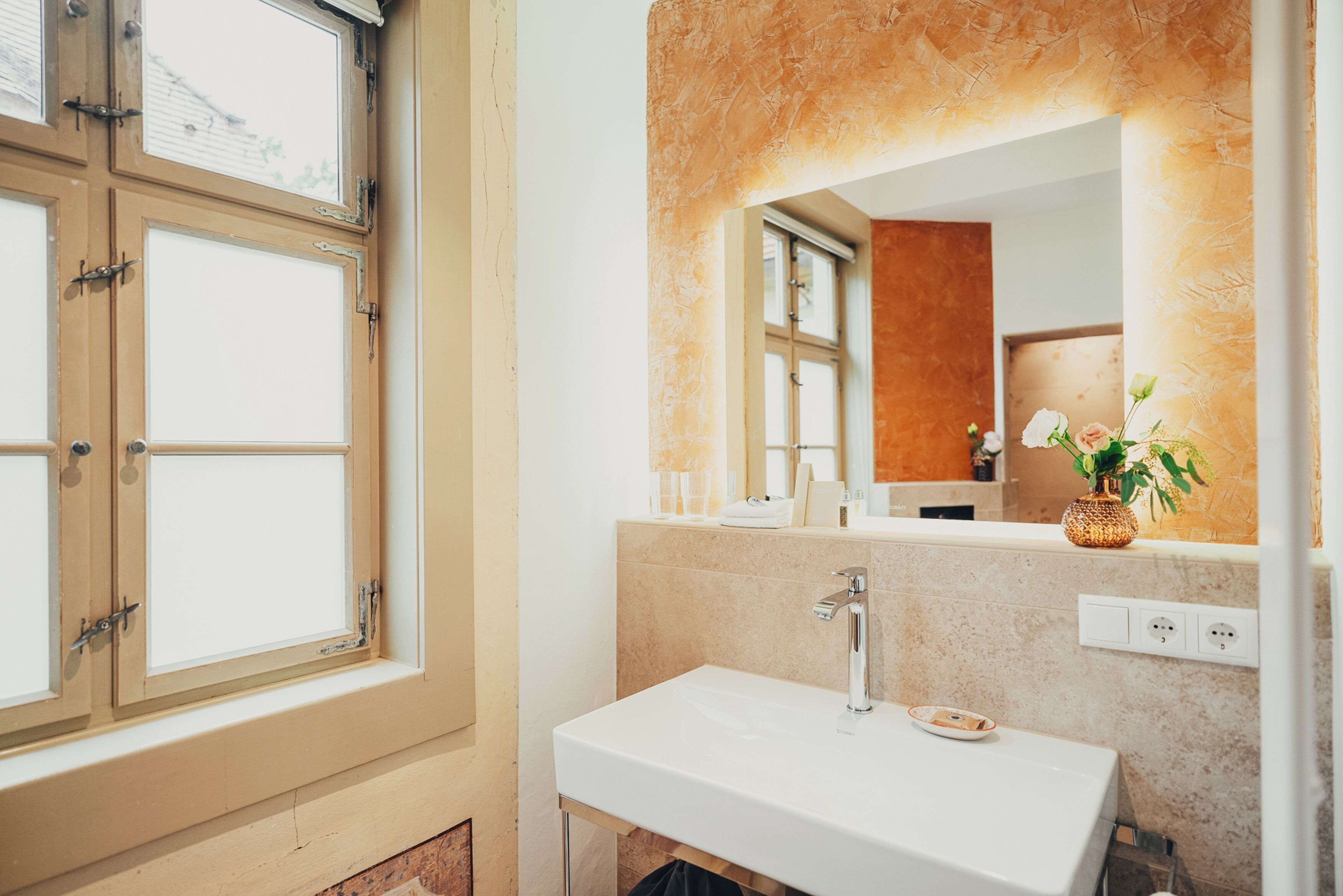 A bathroom with a white sink, a mirror, and a window.