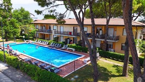 Una piscina con sillones de descanso, rodeada de árboles y un edificio con balcones.