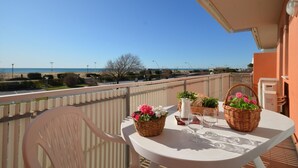 Un balcon avec une table dressée pour deux personnes, offrant une vue sur la mer et un ciel dégagé.