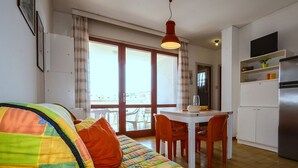A cozy living room with a colorful quilted sofa, a dining table with chairs, a kitchen area with a refrigerator, and a balcony with a view. - Centric and comfortable retreat (Bibione)