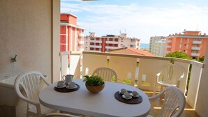 A balcony with a table set for two, white plastic chairs, and a view of buildings in the background. - Centric and comfortable retreat (Bibione)