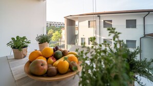 A balcony with a wooden bowl of fruit, potted plants, and a view of a modern building.