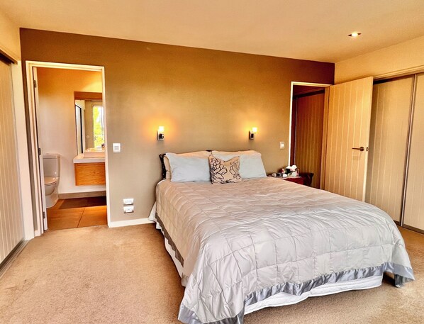 A bedroom with a large bed, two bedside tables, a nightstand, a mirror, and a door leading to a bathroom.