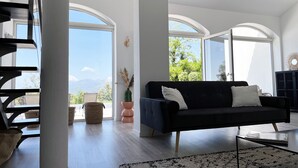 Un salón espacioso con un sofá azul oscuro, una mesa de centro y un ventanal con vistas a zonas verdes y montañas.