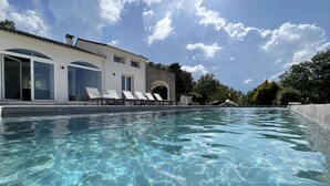 Una piscina cristalina con sillas de descanso y un edificio con amplios ventanales y una entrada arqueada.