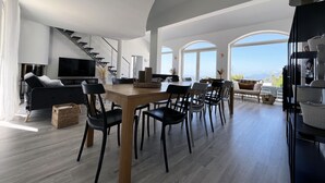 Amplia sala de estar con una mesa de comedor de madera, sillas negras y una escalera moderna.