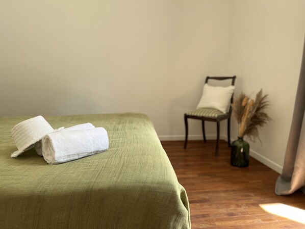 Una habitación con una cama, una silla y un florero con plantas secas.