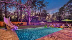 A backyard with a swimming pool, a slide, and a wooden fence. - Luxury Island Home – Pool Oasis, Near Downtown! (Savannah)
