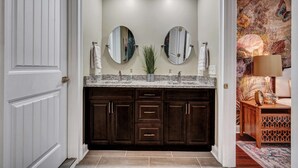 A modern bathroom with dark wood cabinets, a granite countertop, and two round mirrors. - Luxury Island Home – Pool Oasis, Near Downtown! (Savannah)