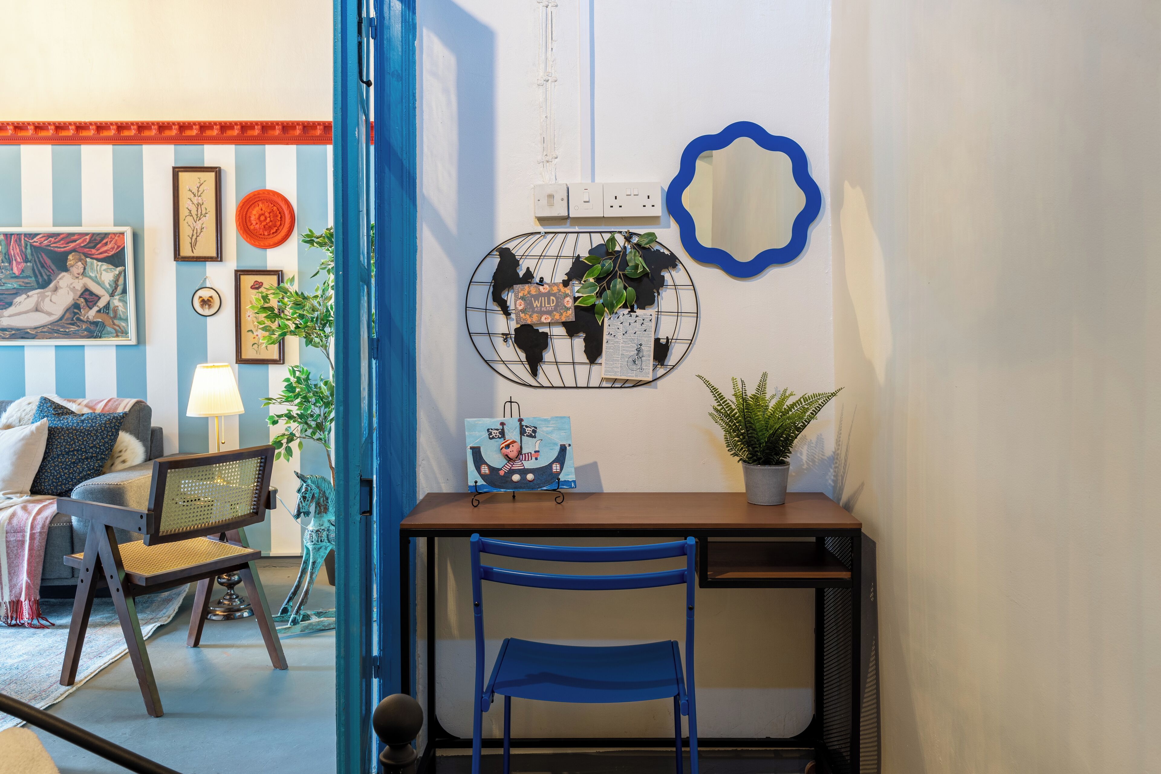 A room with a striped wall, a desk with a chair, a globe, and a potted plant.