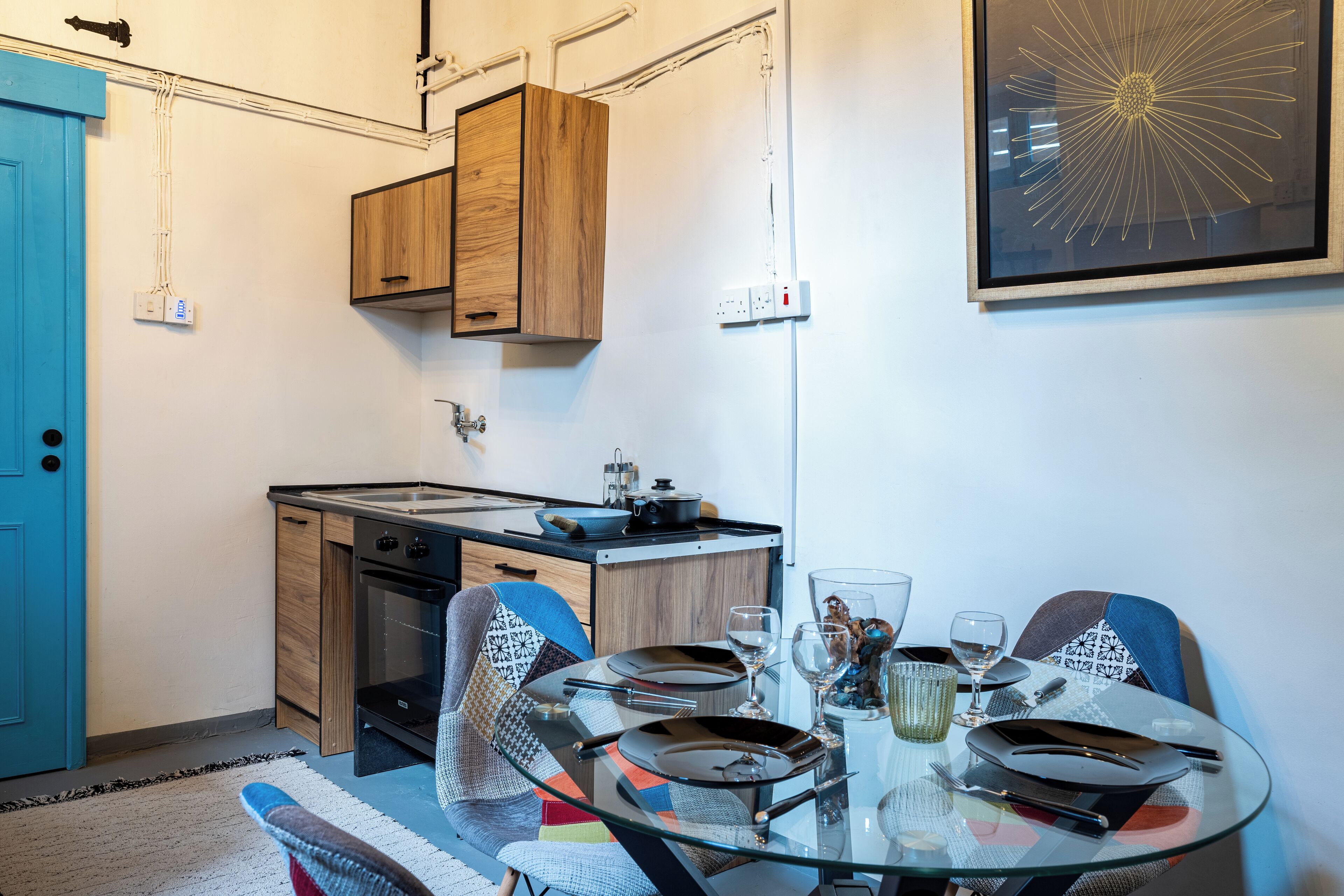 A compact kitchen with wooden cabinets, a stove, and a small dining area with a glass table set for two.