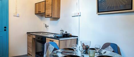 A compact kitchen with wooden cabinets, a stove, and a small dining area with a glass table set for two.