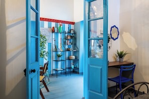 A room with a blue door, a wooden desk, a blue chair, and a metal shelf unit with various items. - Blue Haven - 2 Bedroom Escape in Larnaca (Larnaca)