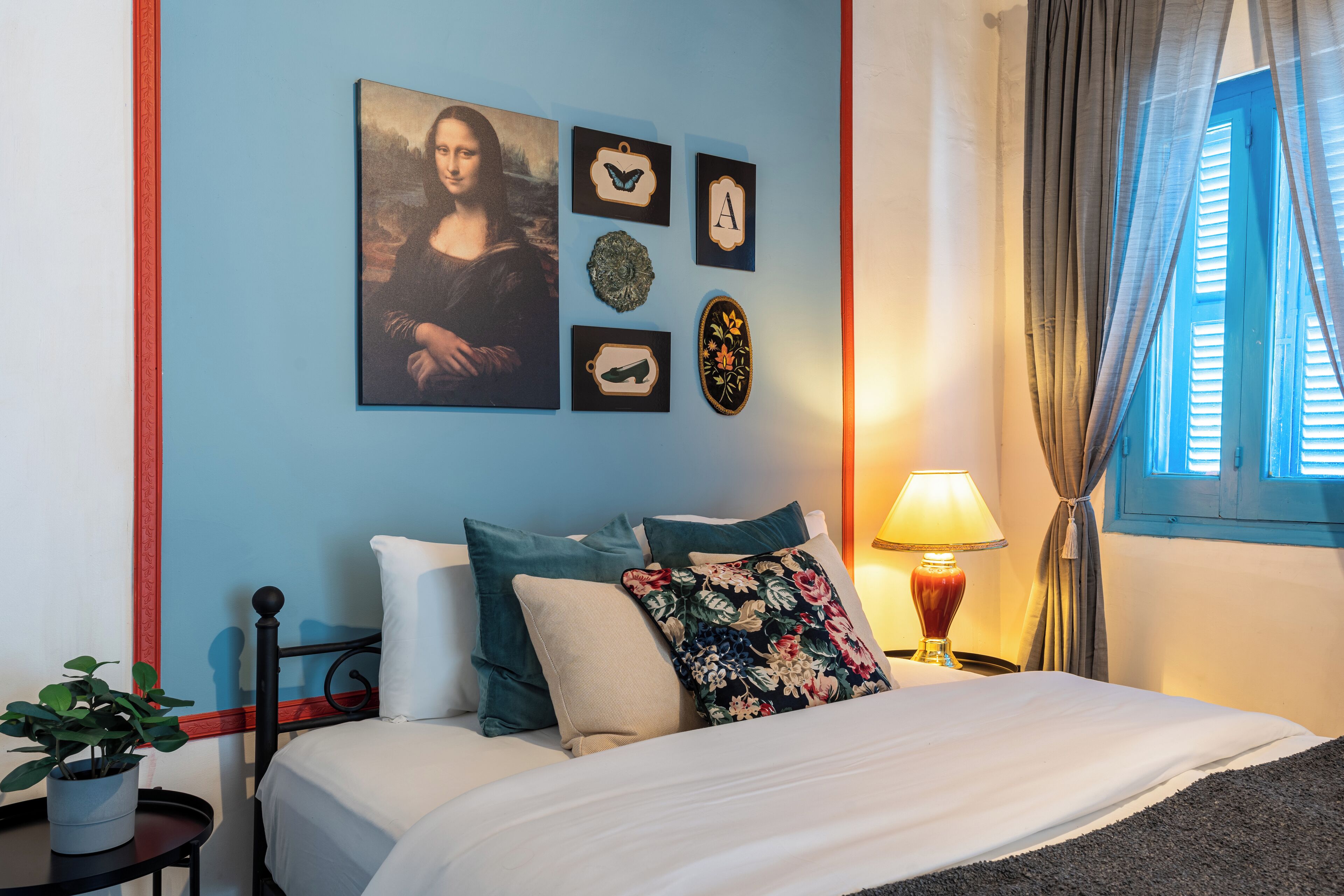 A bedroom with a bed, a nightstand, a lamp, and a wall with artwork.