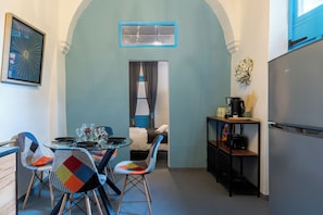 A compact kitchen with a dining area, featuring a small table with chairs, a refrigerator, and a coffee machine. - Blue Haven - 2 Bedroom Escape in Larnaca (Larnaca)