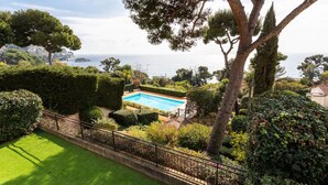 A pool surrounded by well-maintained hedges and trees, with a view of the sea. - LA SOLEILLADE VI4451 By Riviera Holiday Homes (Eze)
