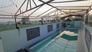 Une piscine couverte, dont le sol et les murs sont recouverts de carrelage, et qui est entourée d’une structure métallique.