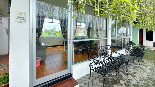 Un espace extérieur aménagé avec des chaises et des tables en métal, une entrée avec une porte en verre et des plantes suspendues.