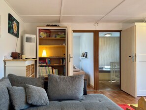Un salon comprenant un canapé, une bibliothèque, un radiateur et une porte donnant sur une autre pièce.
