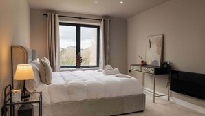 Een moderne slaapkamer met een groot bed, een nachtkastje met een lamp, een zwarte tv-meubel en een raam met gordijnen.