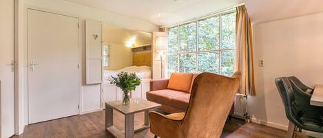 A modern room with a wooden floor, a brown leather chair, a small table with a vase, and a window with curtains.