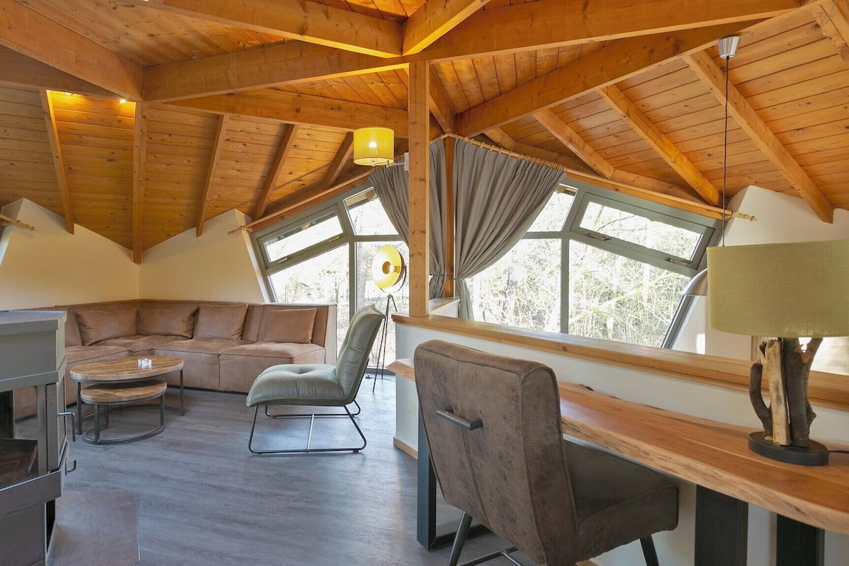Un interior acogedor de cabaña con techo de madera, un sofá, una mesa de comedor y una chimenea.