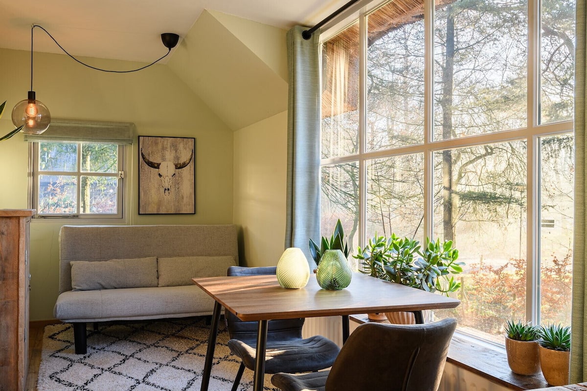 Una habitación acogedora con una mesa de madera, un banco acolchado y un ventanal con vistas a árboles.