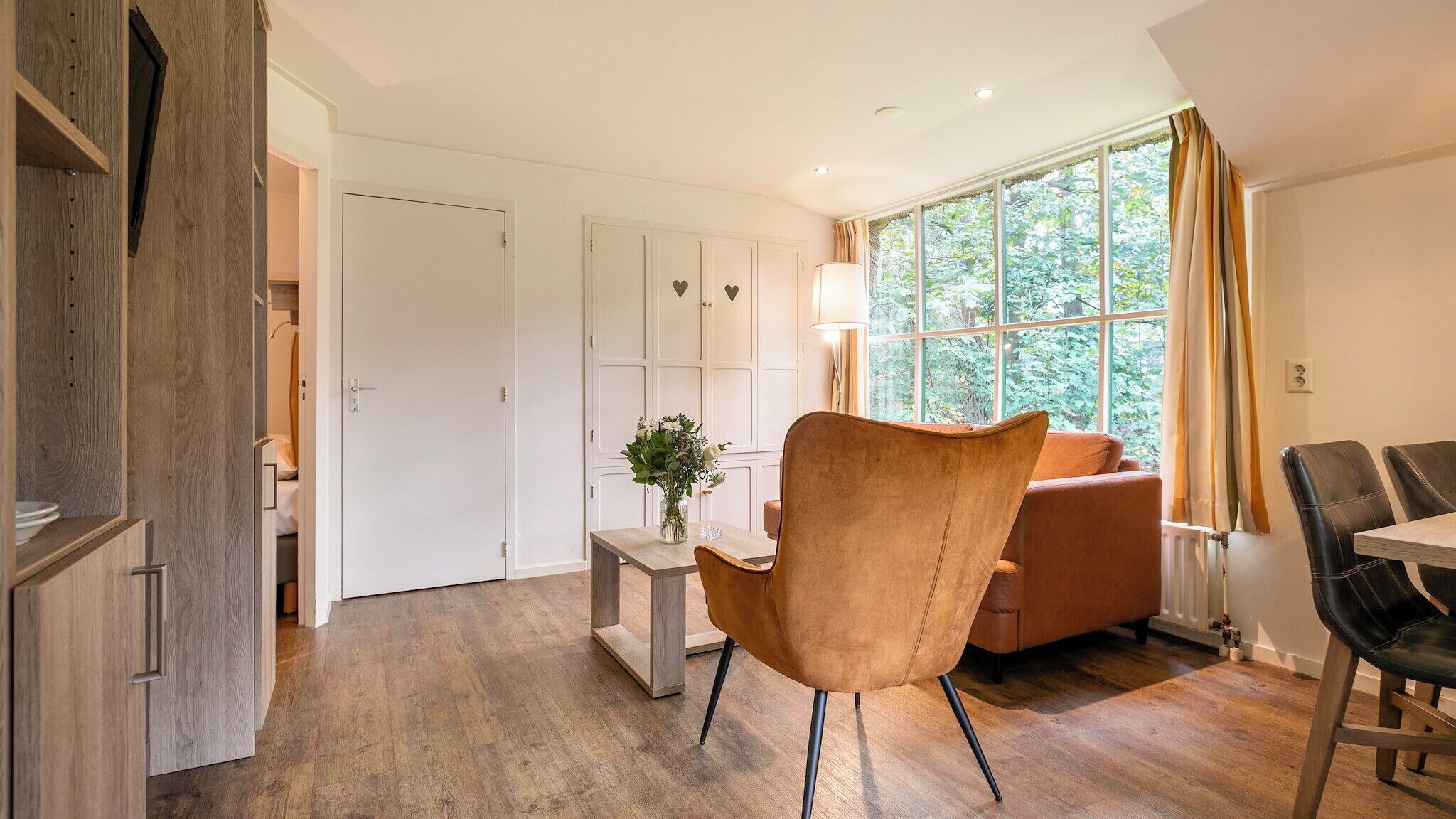 A modern room with a wooden floor, a brown leather chair, a wooden table, a sofa, and a window with curtains.