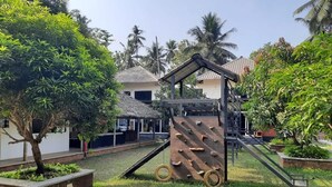 Ein Spielplatz mit Kletterwand und Rutschen, umgeben von viel Grün und Palmen.