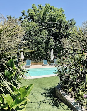 A pool area with a clear view of the pool, surrounded by lush greenery and a metal archway. - CHARMING FARMHOUSE WITH WOODED GROUNDS AND SWIMMING POOL (Avignon)