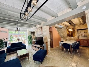 A spacious living area with a sofa, a coffee table, a TV, and a dining area with chairs and a table. - CHARMING FARMHOUSE WITH WOODED GROUNDS AND SWIMMING POOL (Avignon)