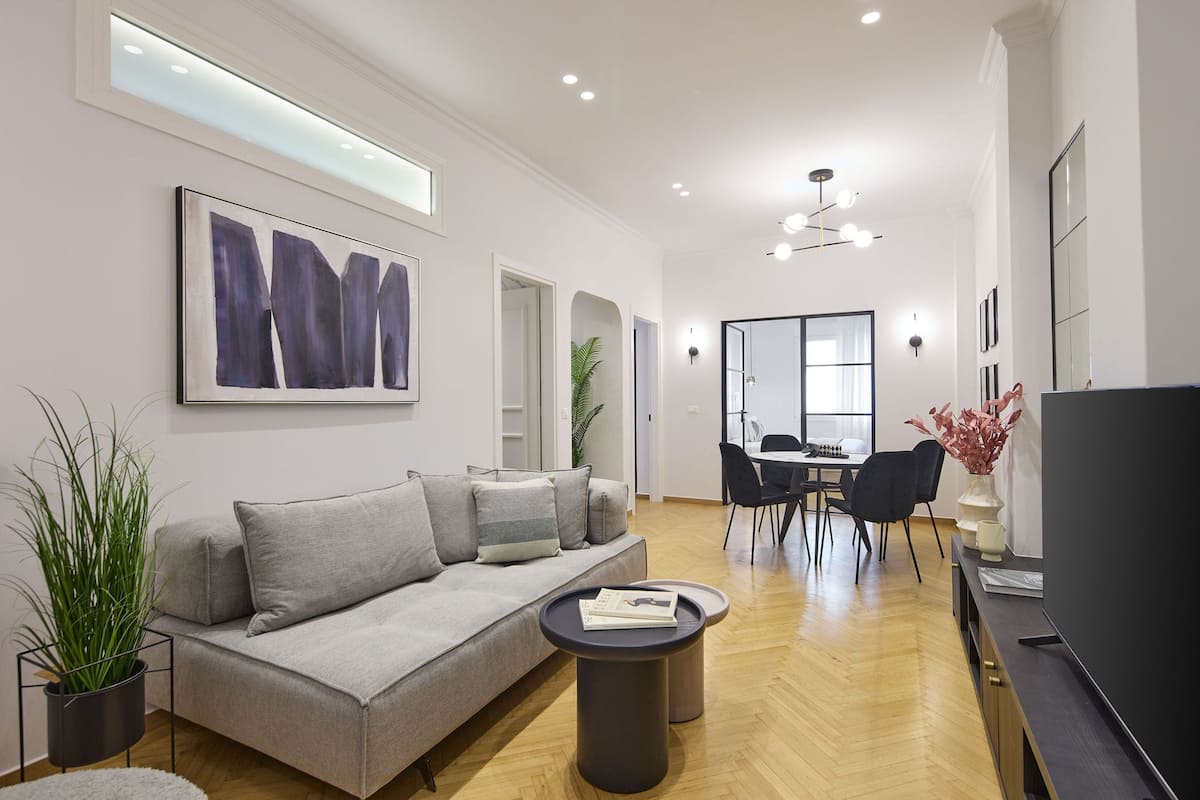 A modern living room with a grey sofa, a coffee table, and a dining area with chairs and a table.
