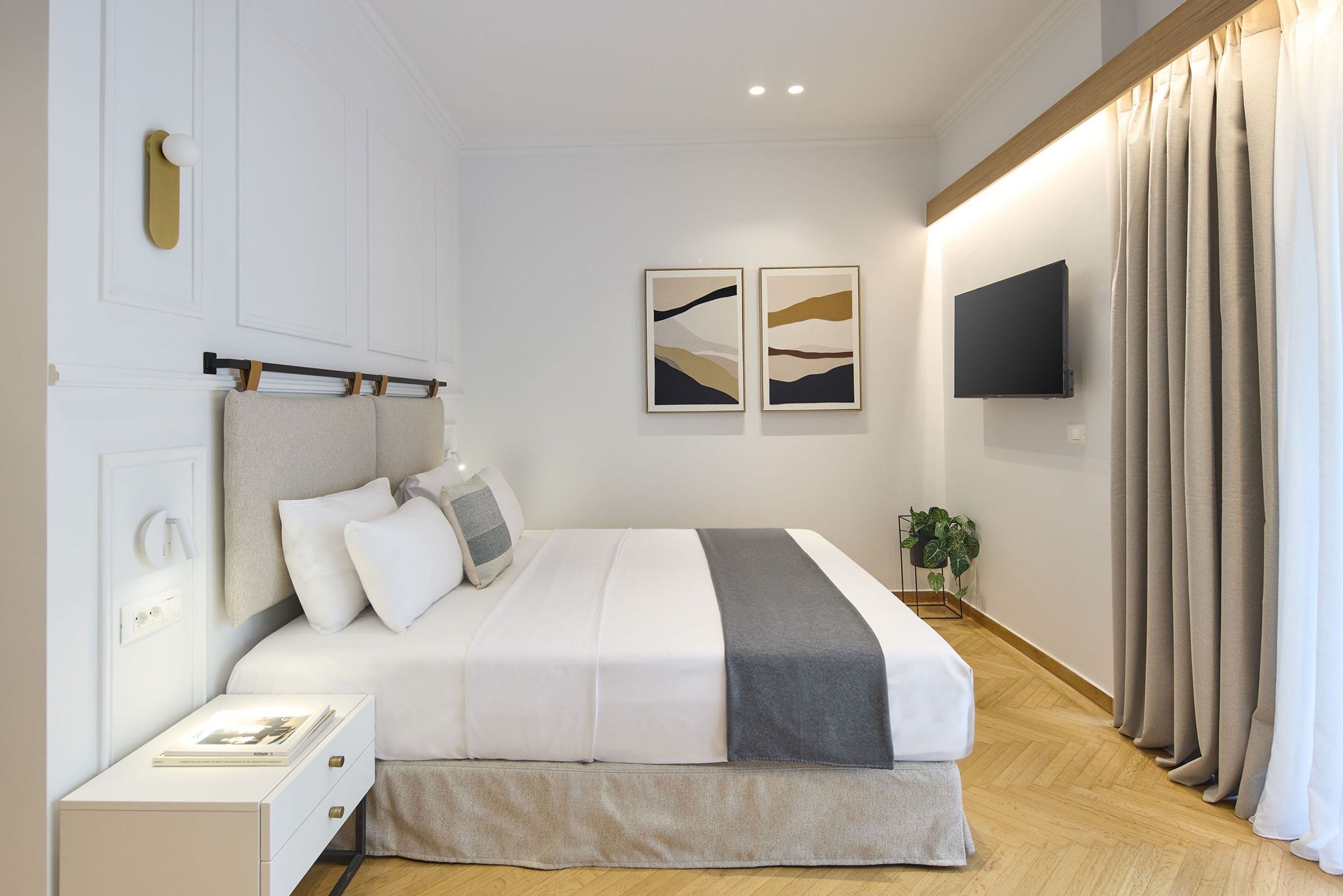 A modern bedroom with a bed, bedside table, wall-mounted TV, and artwork.