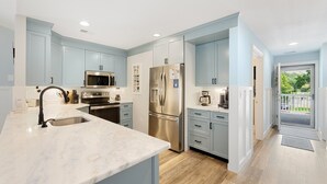 A modern kitchen with light blue cabinets, stainless steel appliances, and a marble countertop. - Heart of Pawleys Island 3BR Golf Condo Across from Pool (Pawleys Island)