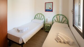 Una habitación con dos camas individuales, una mesita con una lámpara, un cuadro en la pared y una ventana.