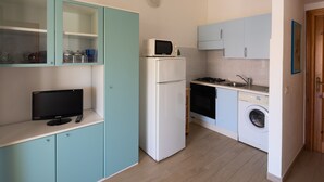 A compact kitchen with a refrigerator, microwave, stove, sink, and washing machine. - Sabbia Marina (Budoni)