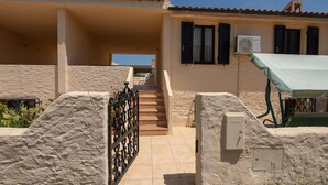 A residential building with a staircase leading to a balcony, a covered outdoor seating area, and a utility box on the ground. - Resinosa in Agrustos (Budoni)