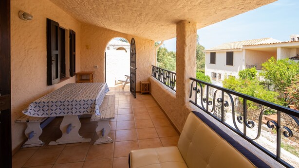 A balcony with a bed, a chair, and a view of the surrounding buildings and greenery. - Resinosa in Agrustos (Budoni)