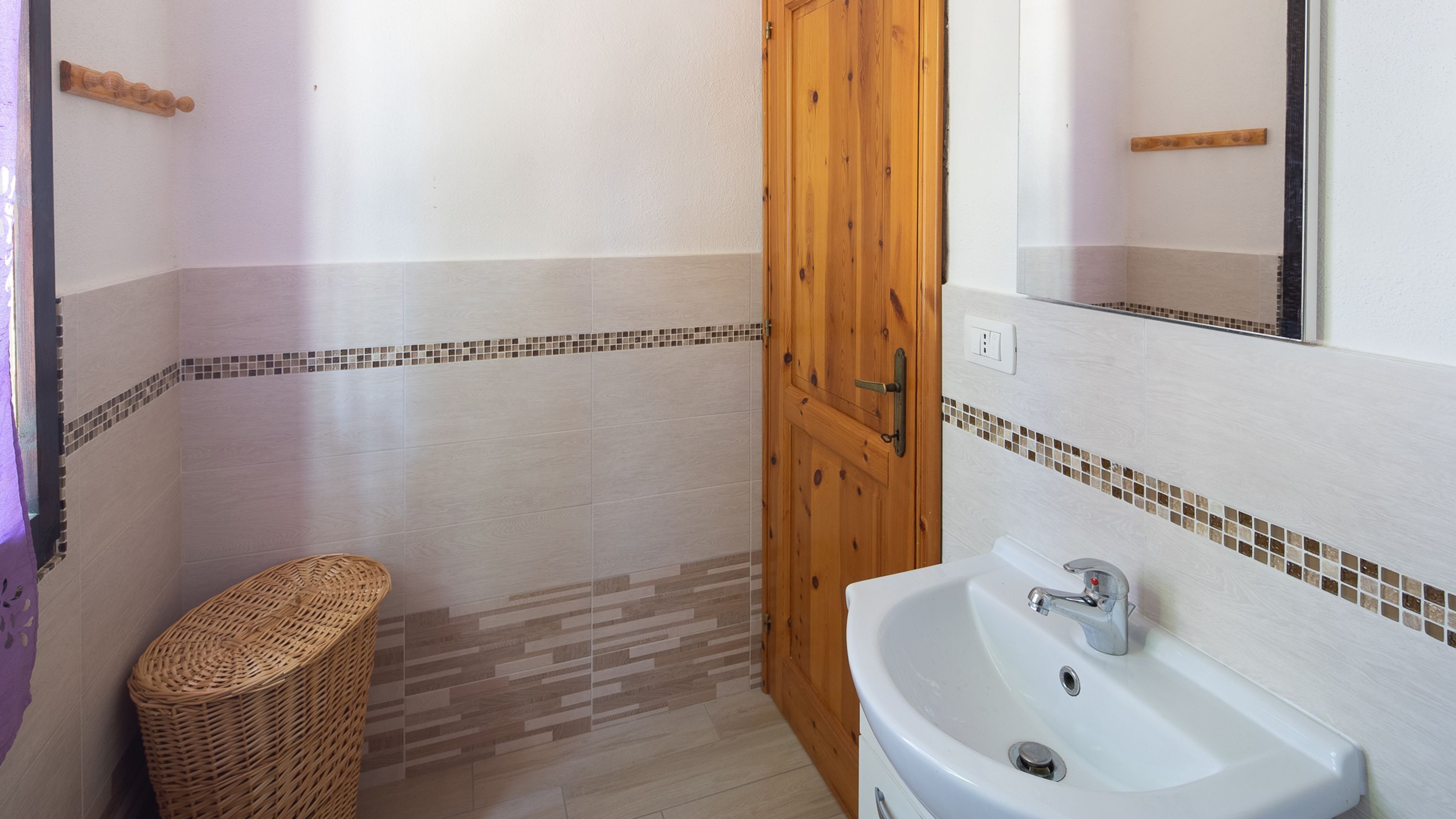 A bathroom with a wooden door, a white sink, and a tiled floor.