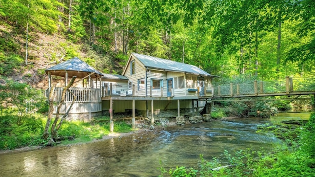 A cabin with a porch and a small gazebo, built over a stream in a forested area. - Splash at the Creek, roast marshmallows & play ping-pong together – Wade 'N Bear (Sevierville)