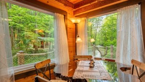 A wooden dining table with chairs, a lamp, and a view of a lush forest through large windows. - Splash at the Creek, roast marshmallows & play ping-pong together – Wade 'N Bear (Sevierville)
