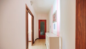 Un pasillo estrecho con una puerta de madera al final, un mostrador blanco con lavamanos y un suelo con diseño.
