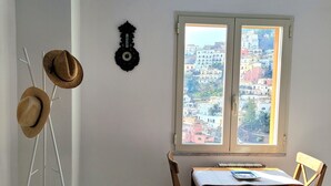 A dining area with a table and chairs, a window with a view of colorful buildings, a hat rack, and a decorative wall clock. - Elle, a stone's throw from the Sea (Positano)