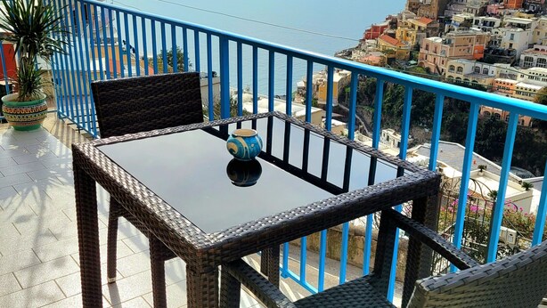 A balcony with a table and chairs, overlooking a coastal town with colorful buildings. - Elle, a stone's throw from the Sea (Positano)