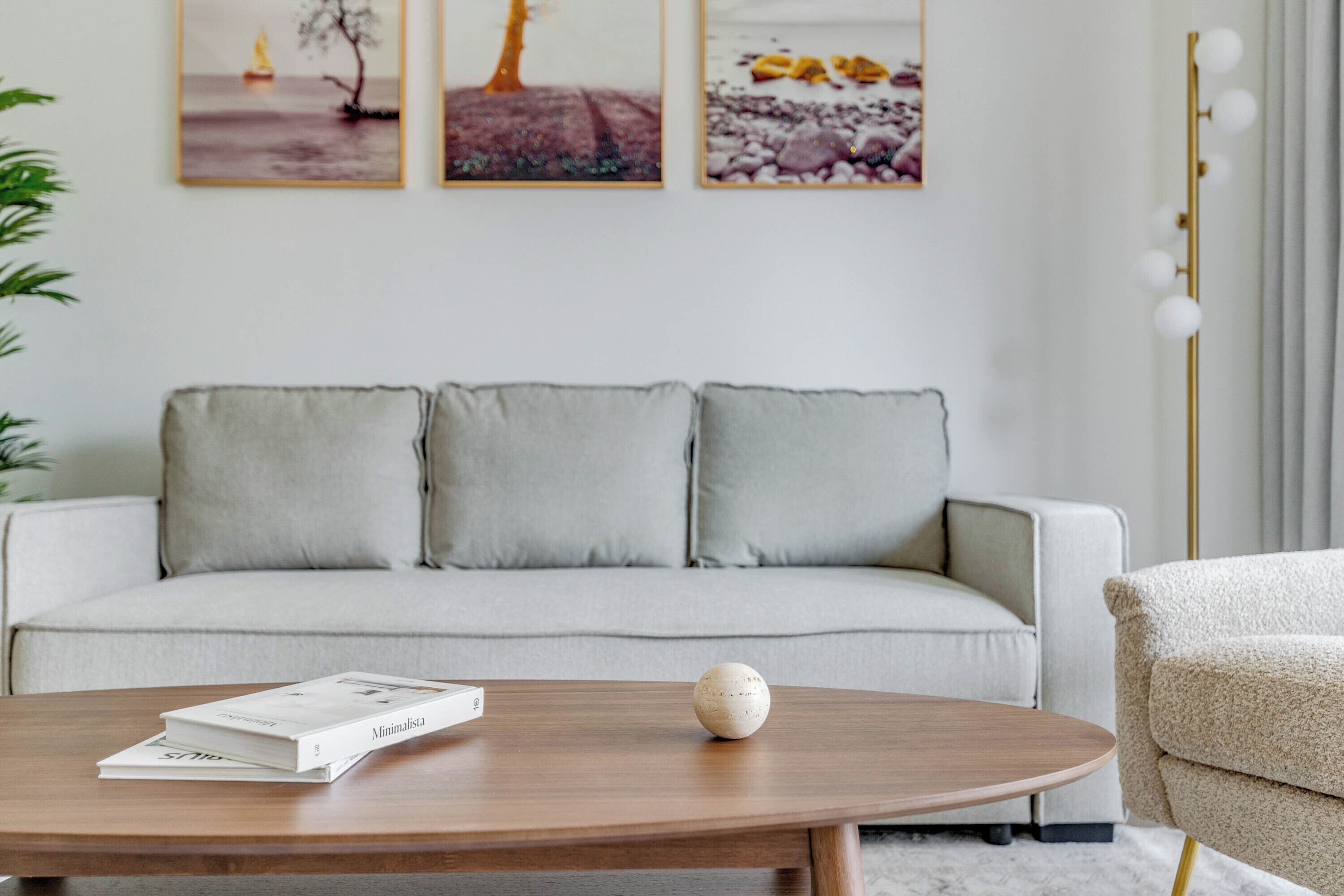 En moderne stue med en grå sofa, et træsofabord med en bog og en pynteting, samt tre billeder hængende på væggen.