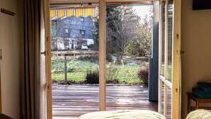 Ein Zimmer mit einer Schiebeglastür, die auf eine Terrassenfläche nach draußen führt.